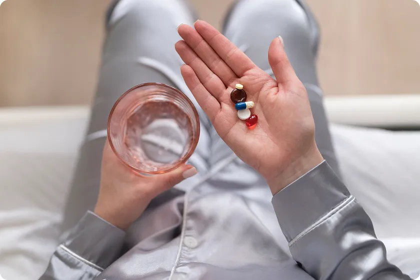 A close-up of a hand holding different pills with a glass of water, reflecting the daily medication routine for lupus patients dealing with the autoimmune disease and lupus cancer.