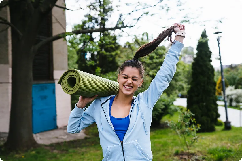 Woman carrying yoga mat after tension relieving exercises outdoors for skin-friendly habits.